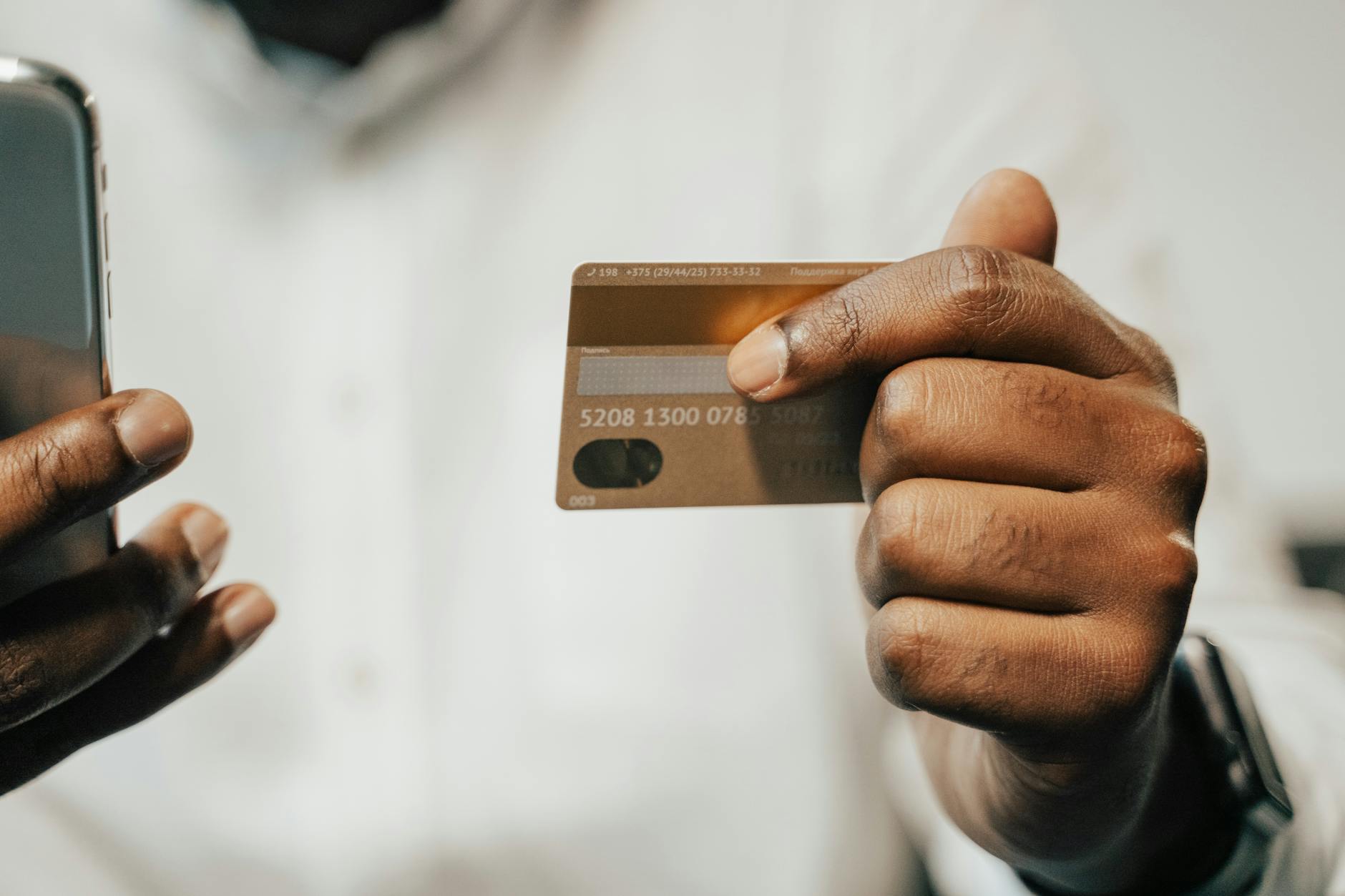 A person holding a credit card while checking account details on a phone.