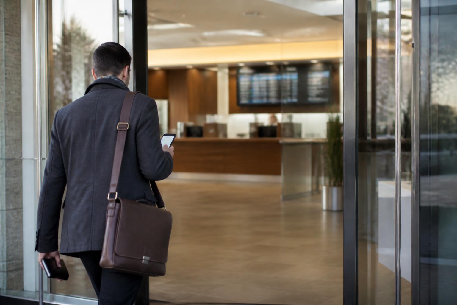 A commuter entering a bank lobby while checking a blurred banking alert.