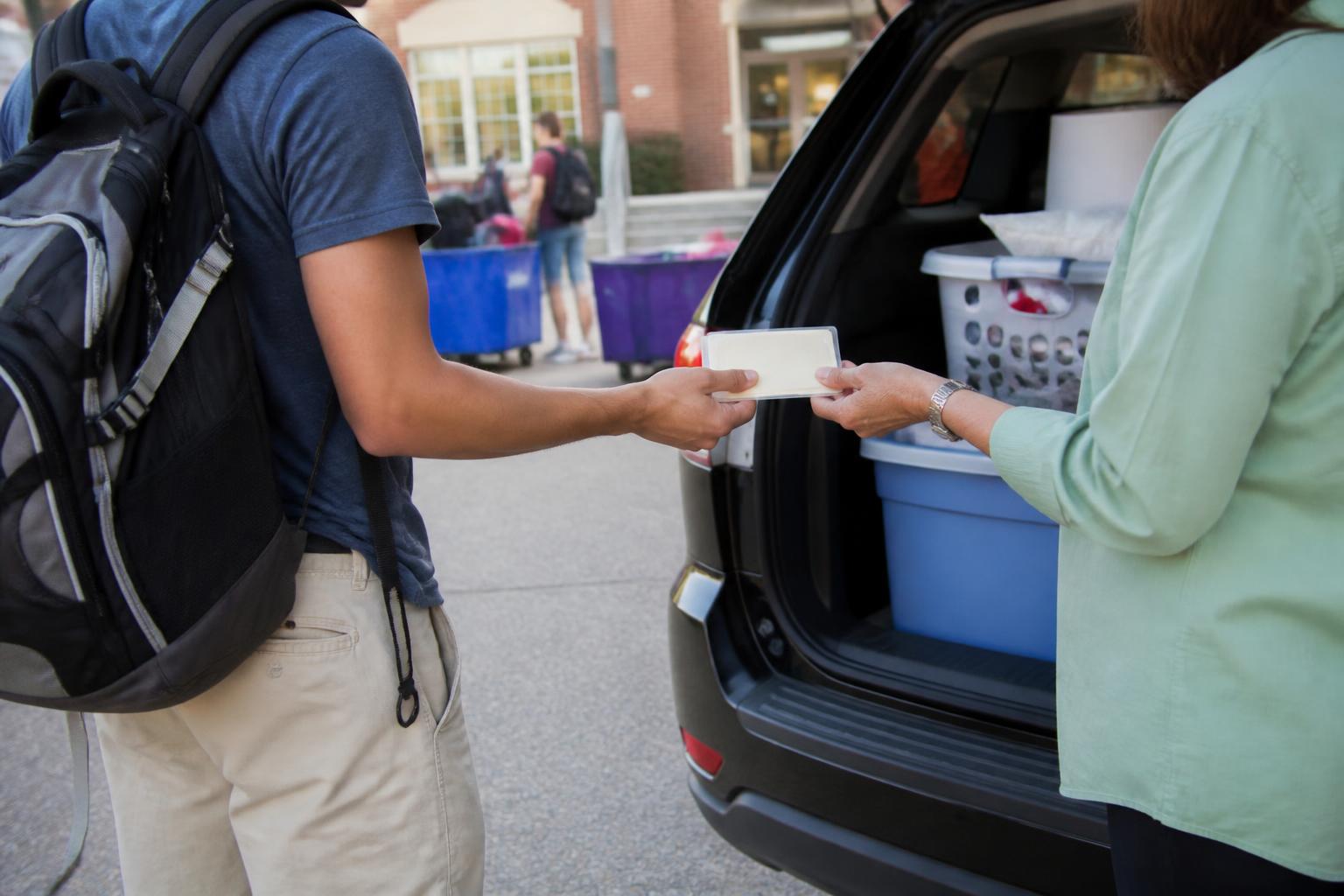 A parent handing a card sleeve to a student during campus move-in.