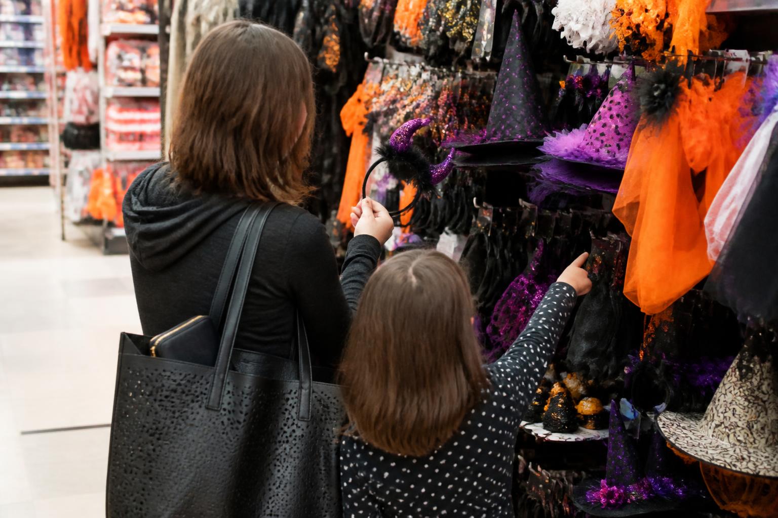 A parent and child choosing one plain Halloween costume accessory in a store aisle.