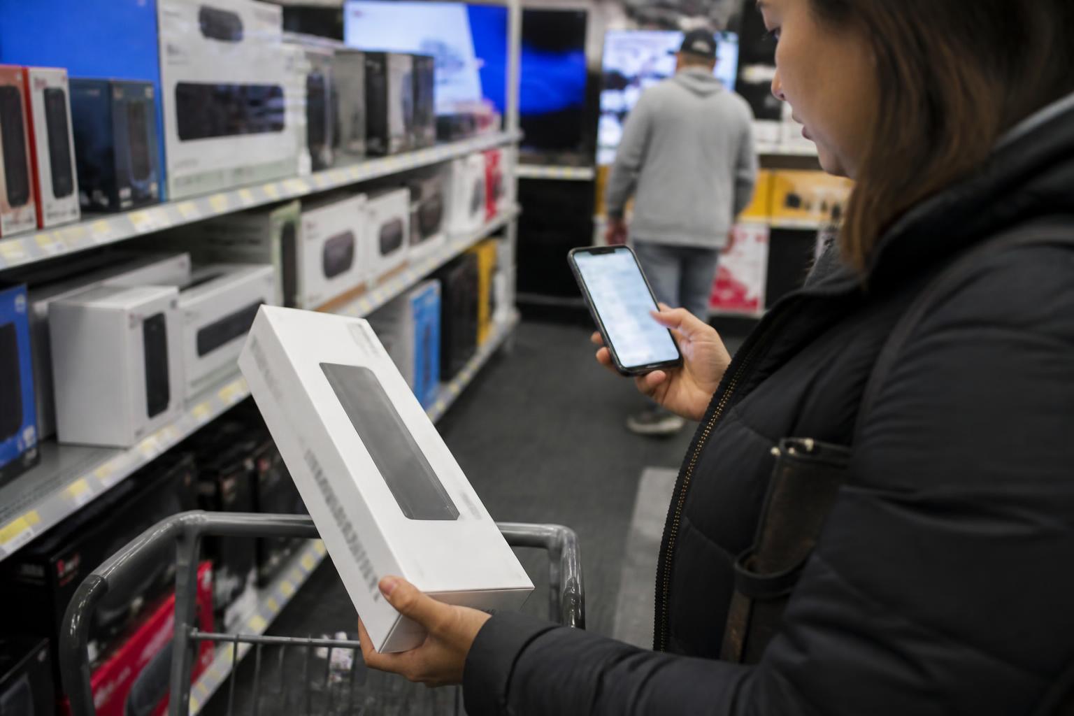 A shopper stepping aside from a display to turn on a blurred card alert before picking up a box.