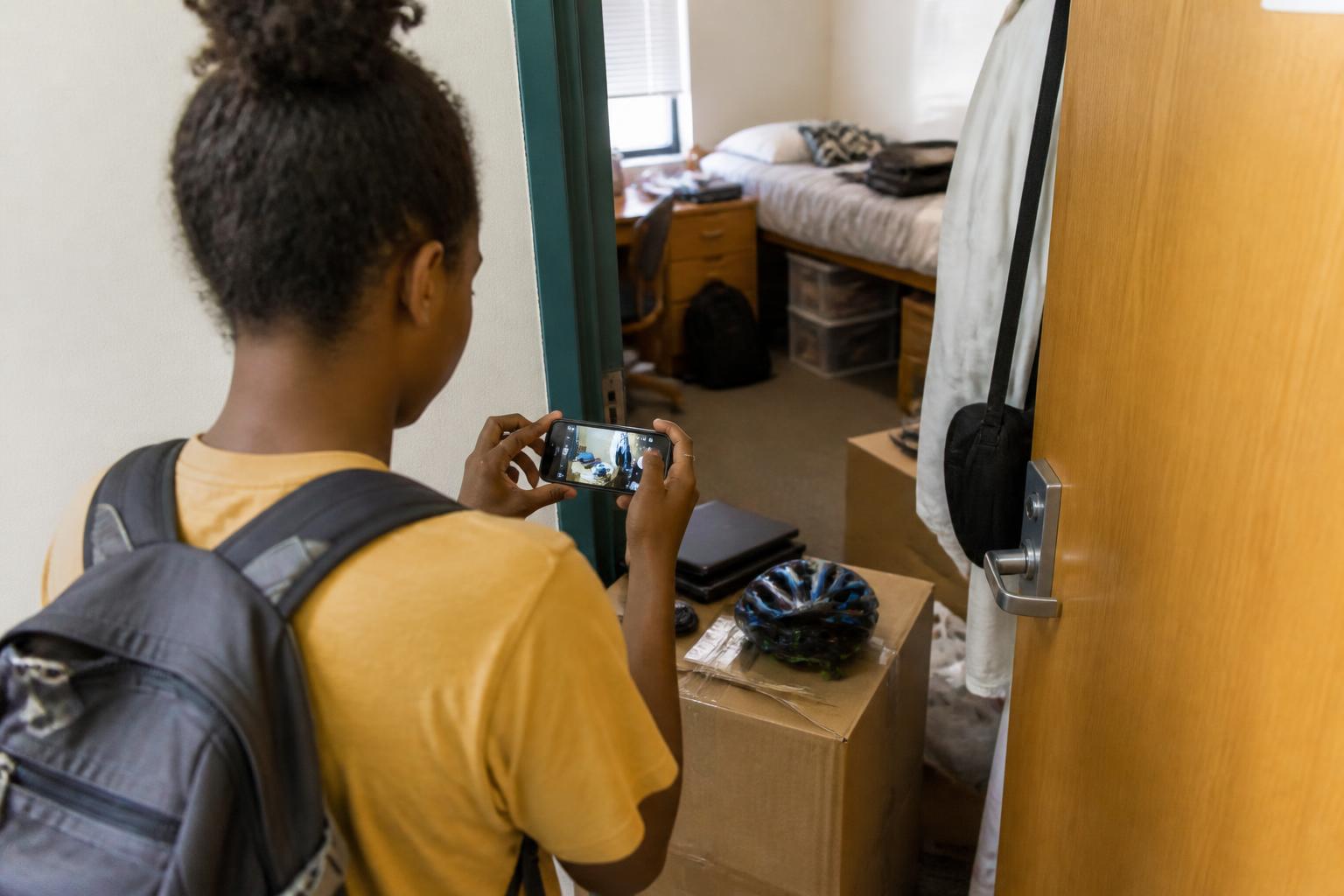 A student photographing move-in belongings in a dorm hallway.