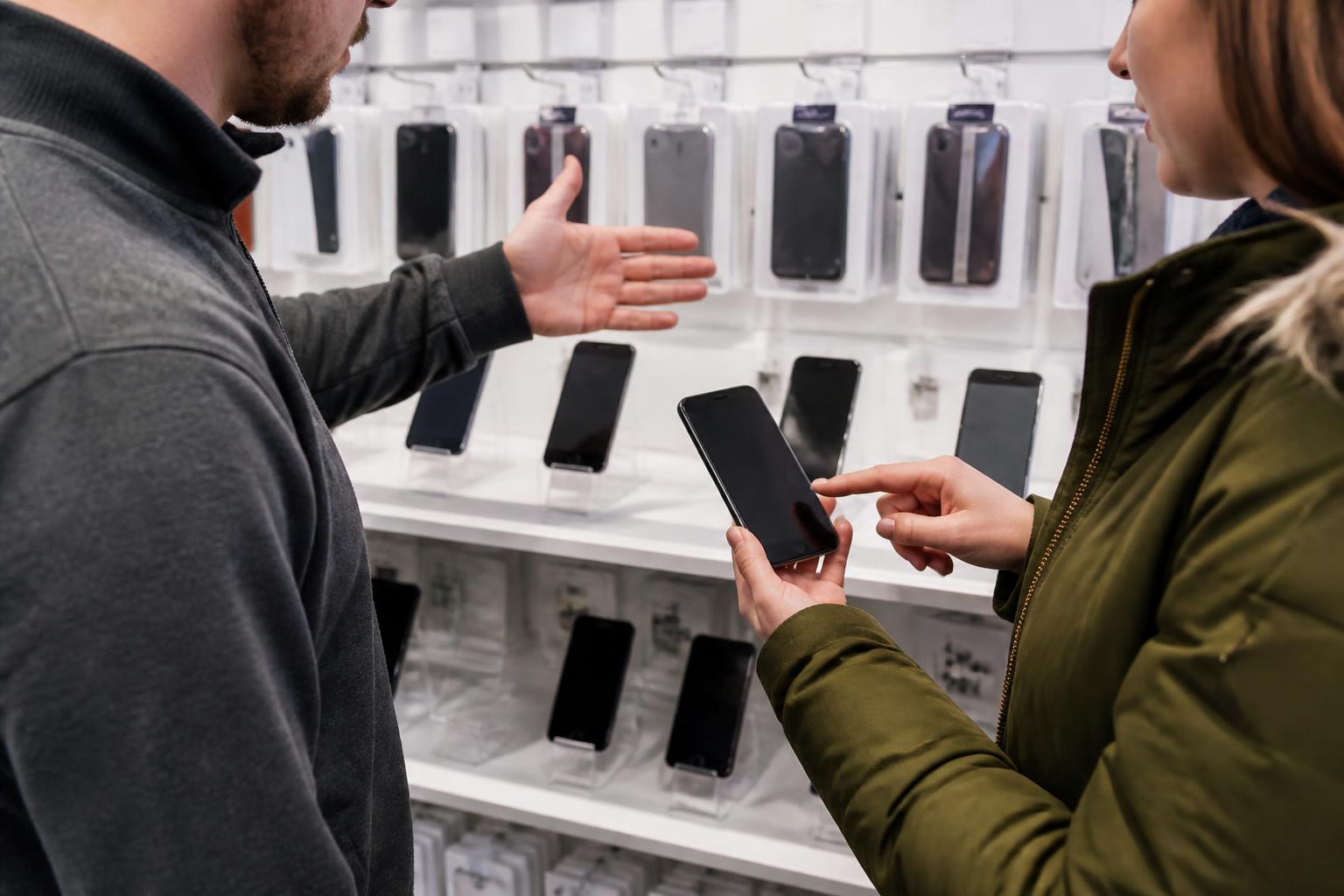 A customer pointing to an unused older phone while a representative gestures toward device shelves.