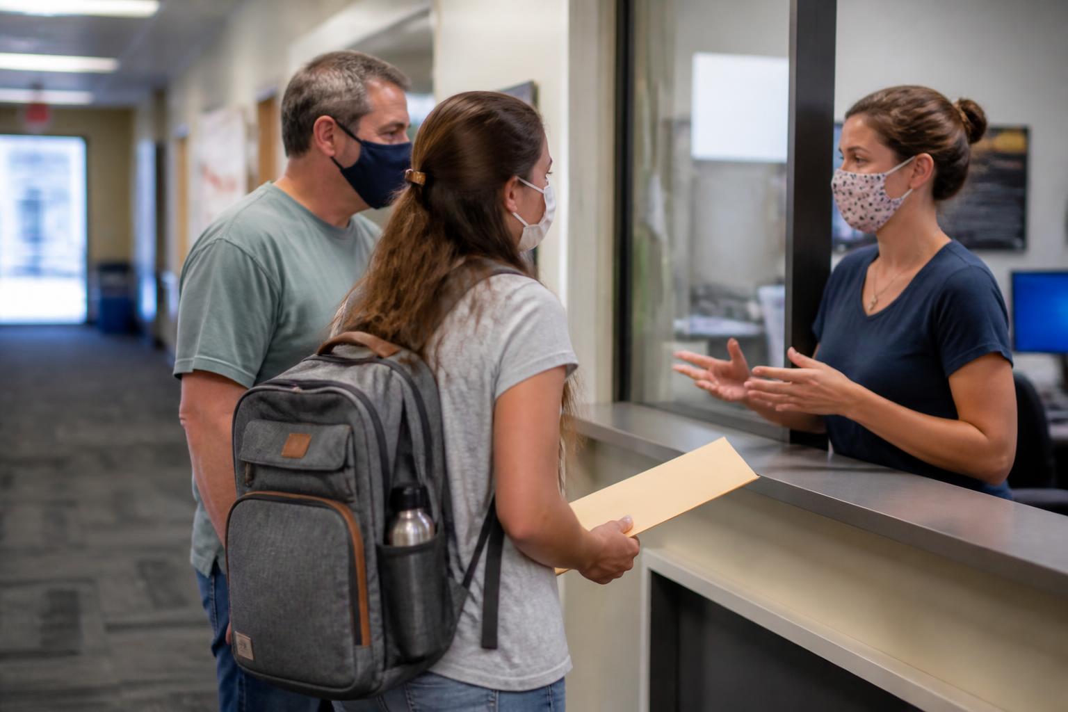 A student and parent asking about a housing contract in a campus office hallway.