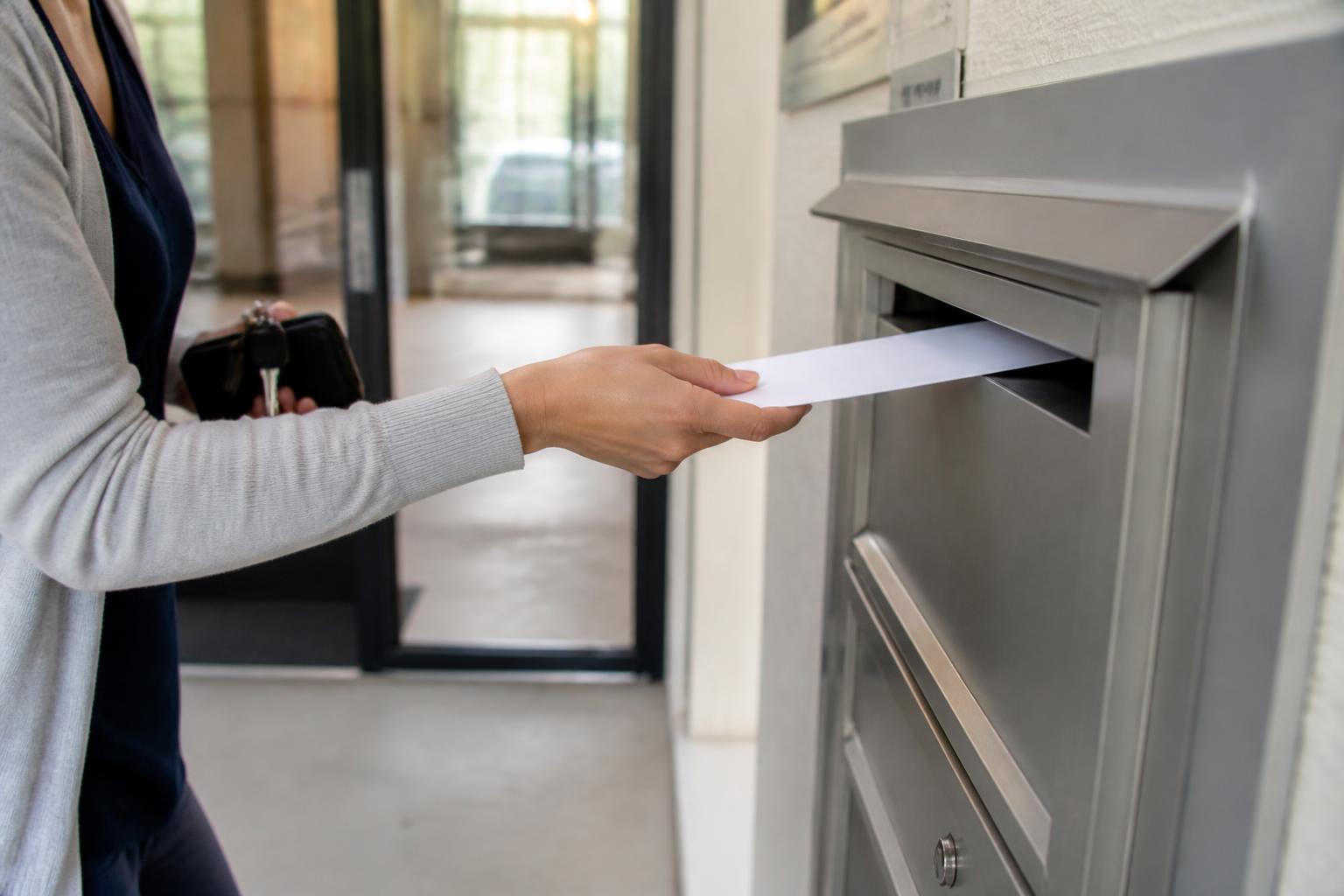 A renter placing a sealed envelope into an apartment rent drop box.