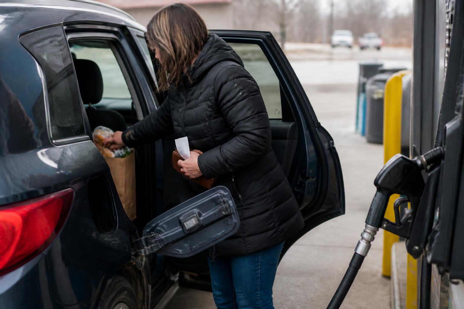 A driver loading groceries beside a fuel pump.