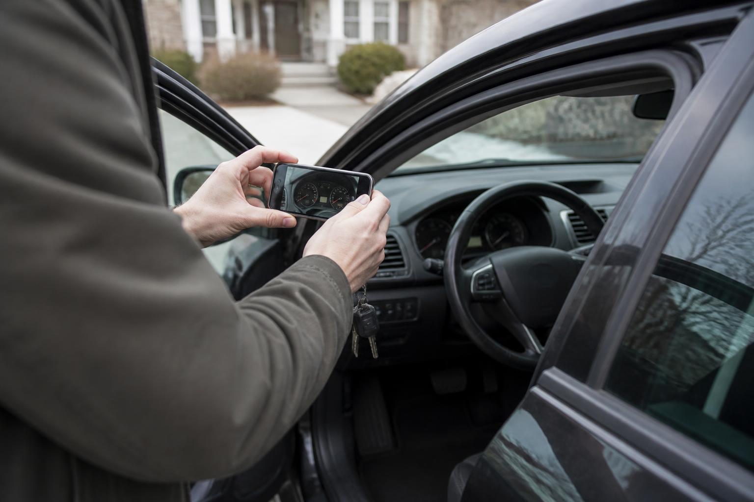 A driver photographing mileage through an open car door.