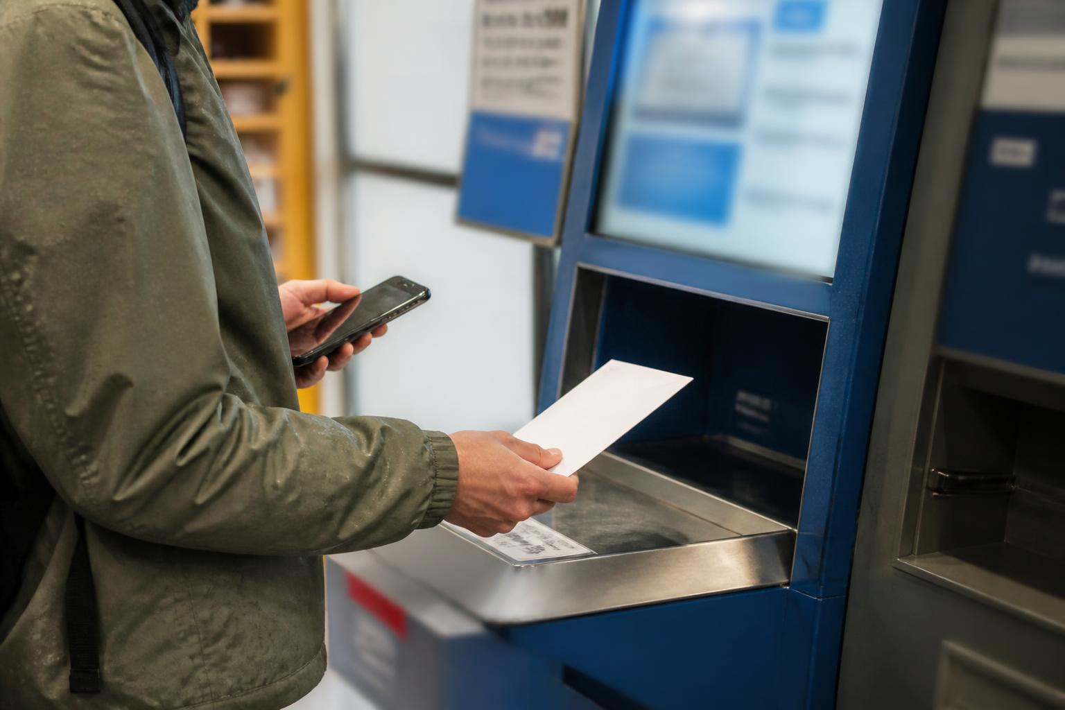 A taxpayer weighing a sealed envelope at a post office kiosk.